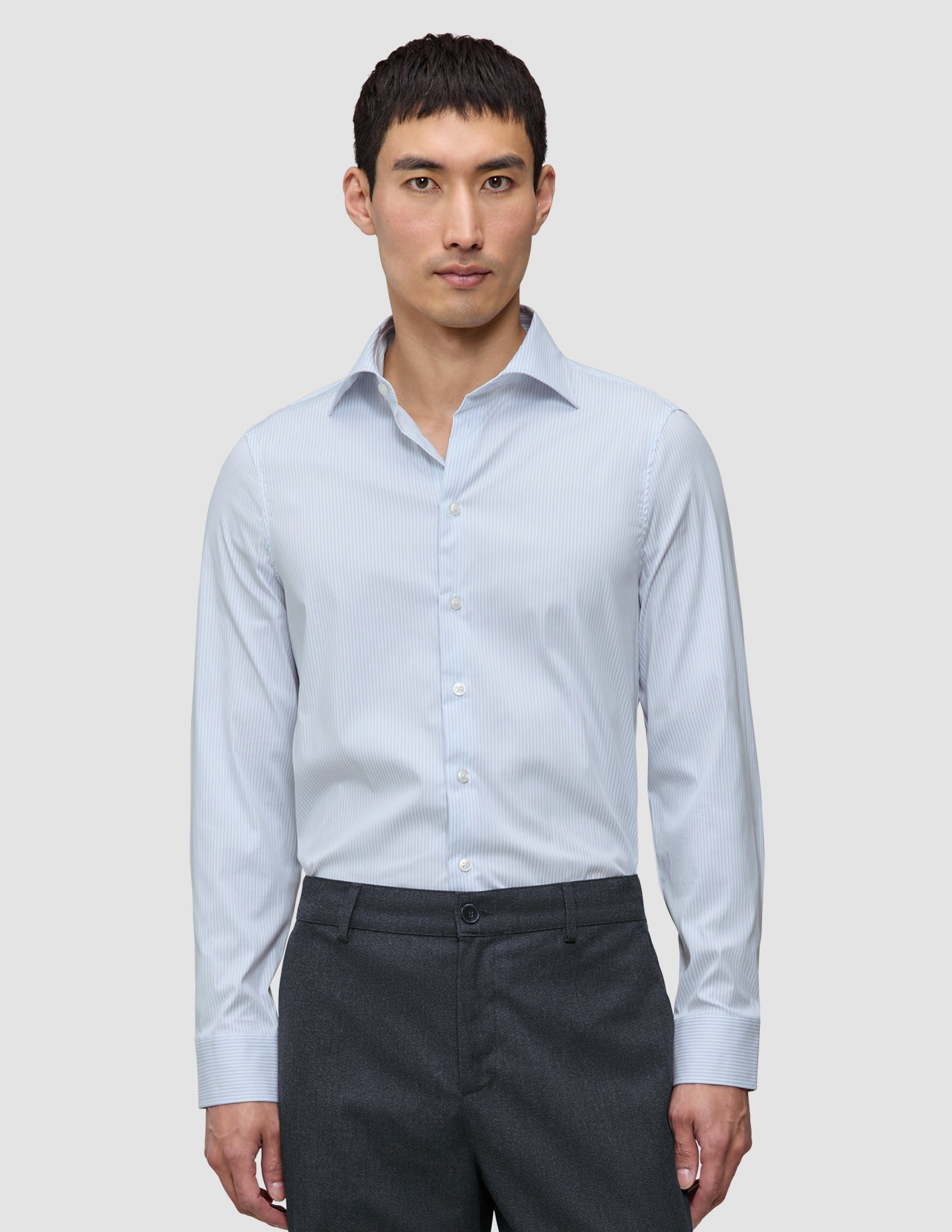 En man i en ljusblå och vitrandig Elevated Shirt Slim Classic Blue Striped tillsammans med mörkgrå byxor.